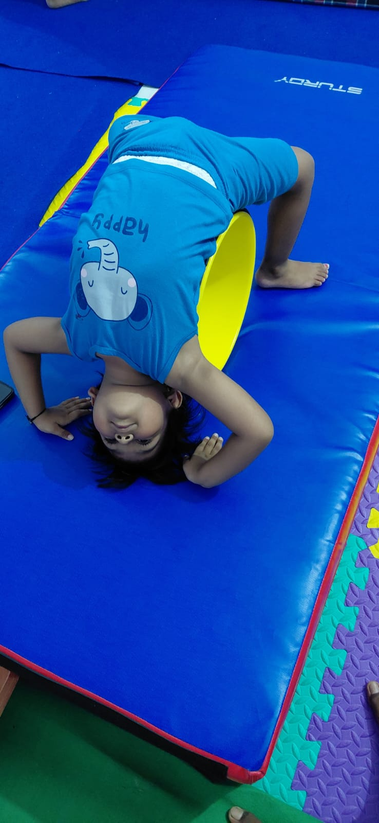 A child practicing a backbend over a padded gymnastics barrel