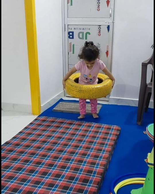 A young child practicing balance with a large tire in the activity room
