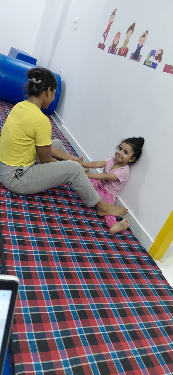 A coach supporting a child during a seated floor stretch
