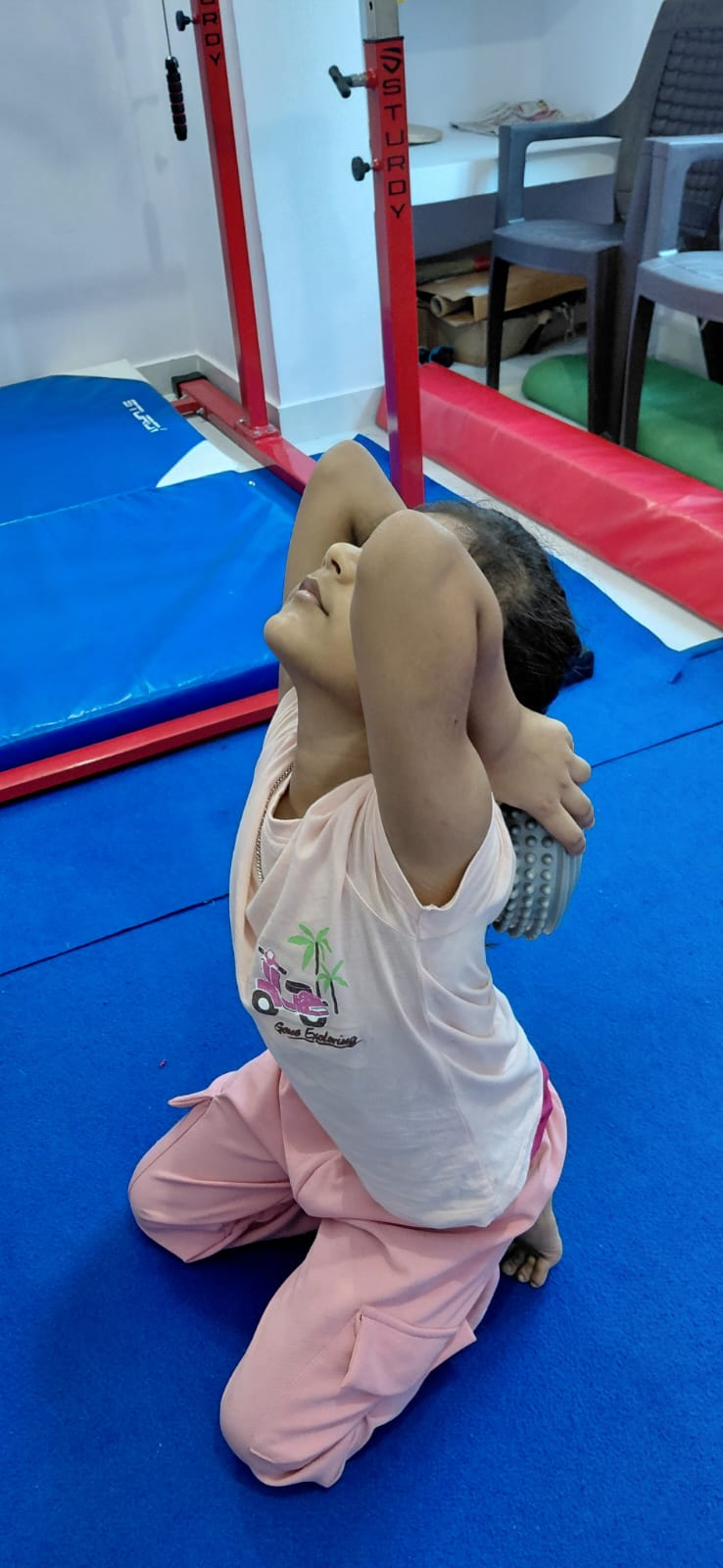 A girl practicing a shoulder flexibility stretch on a padded mat